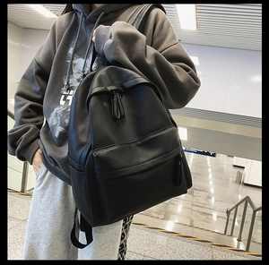 Side view of black lychee grain PU leather backpack worn by a model in casual setting