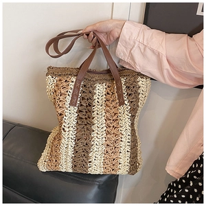 Detail view of woven straw tote bag with vertical stripes and leather shoulder strap