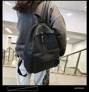 Black pebbled leather backpack with front zipper pocket shown on person in modern staircase