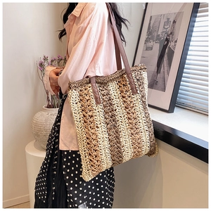 Detail of striped woven straw tote bag with brown leather straps held by a model