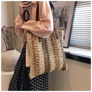 Detailed view of striped woven straw tote with premium brown leather handles and X-stitching
