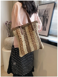 Detail view of woven straw tote bag with vertical stripes and brown leather shoulder straps