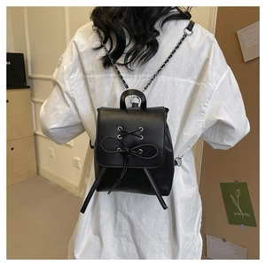 Detail of a mini black PU backpack with ribbon bow design and metal chain straps