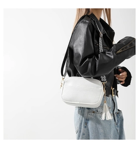 Detail of white lychee leather camera bag with geometric strap and tassel charm