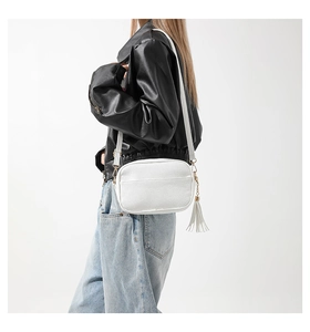 Detail view of white pebbled leather crossbody bag with fringe and slim strap on a model