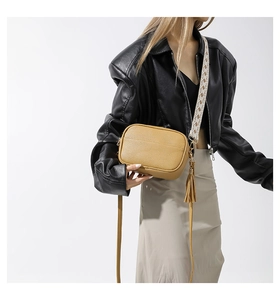 Detail of yellow pebbled leather handbag featuring jacquard strap and tassel charm