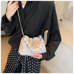 Détail d'une broderie de fleurs en soie rose sur un sac avec anse en perles élégante