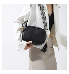 Detail of black pebbled leather crossbody bag with geometric pattern wide strap and tassel