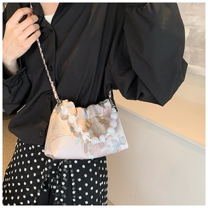 Détail d'un sac bandoulière en soie rose clair avec motif floral et poignée perlée