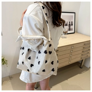 Side view of a large white tote bag with black heart prints worn by a model in a room