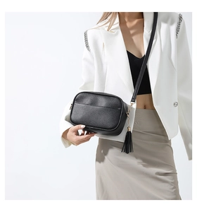 Detail of black pebbled leather crossbody bag featuring stylish fringe and gold hardware