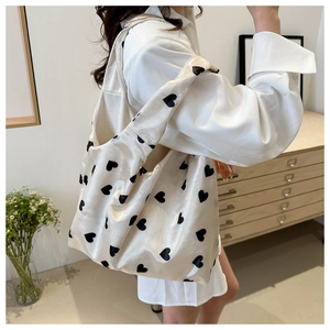 Detail of a silky beige tote bag with black heart prints and wide shoulder strap