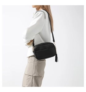 Detail of black lychee grain crossbody bag with leather tassel and metal chain strap