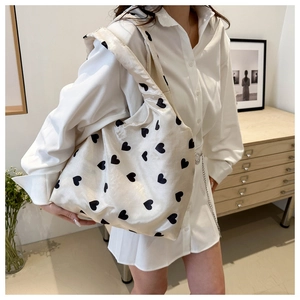 Detail of a creamy white tote bag with black heart patterns in a cozy indoor setting