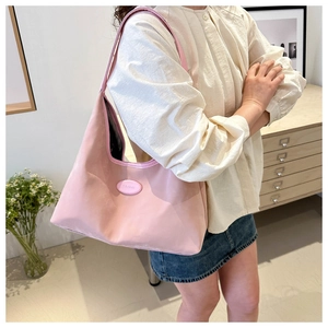Detail of pink PU leather tote bag with logo patch worn by model in casual outfit