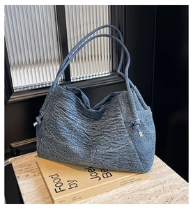 Detail view of denim tote bag with drawstring closure and silver hardware on a book