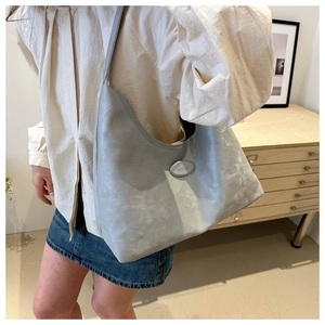 Detail of grey PU leather tote bag with vintage texture and oval logo plaque on a shoulder bag
