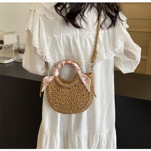 Detail of hand-woven half-moon straw bag with floral silk scarf handle and long strap