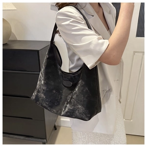 Detail of black faux leather hobo bag with vintage metallic texture and brand plate