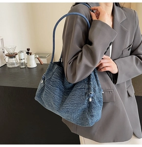 Detail of blue denim tote bag with silver drawstring hardware worn on shoulder