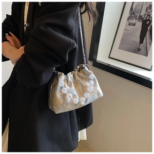 Détail d'un sac à main argenté plissé avec poignée perlée et chaîne sur un mannequin