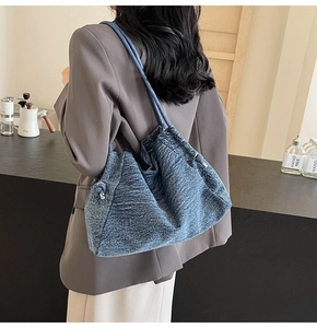 Detail of blue denim tote bag with side metal ring and slender shoulder strap worn by model