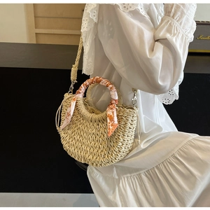 Detail of woven straw handbag featuring decorative silk scarf handle and drawstring