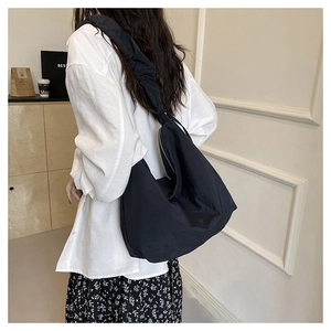 Rear view of a minimalist large black nylon crescent bag with wide pleated strap worn by model