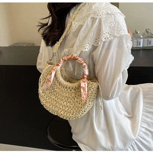 Detail of hand-woven straw crossbody bag with orange silk scarf handle and drawstring closure