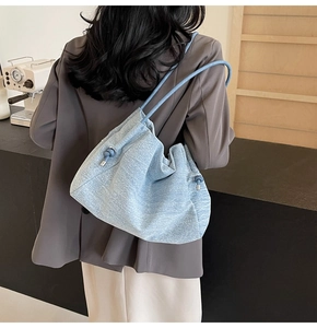 Detail of light blue textured denim shoulder bag with drawstring side and rope strap