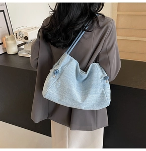 Detail view of a slouchy light blue denim tote bag with drawstring knots on a model