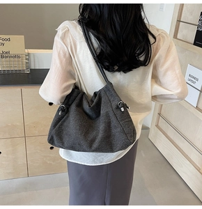 Detail of dark gray hobo shoulder bag with metal knot buckle worn by model