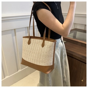 Detail of woven straw tote bag with brown leather trim worn by model in minimalist setting