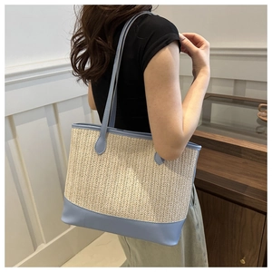 Detail of a large woven tote bag with light blue leather straps worn over the shoulder