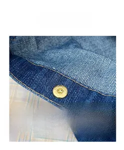 Detailed close-up of brass snap button fastener on premium blue denim fabric texture