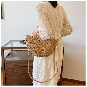 Dettaglio di una borsa a mezzaluna in paglia beige con tracolla intrecciata e manico fisso