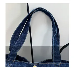 Detail of denim handbag handle with reinforced yellow stitching and metal hardware