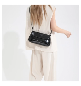Sac bandoulière chic en cuir verni noir porté par le mannequin pour un style élégant