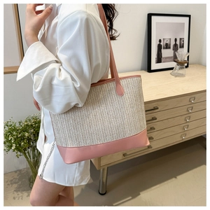 Detail of hand-woven beige tote bag with pink leather straps and metal chain accent