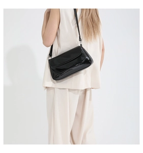 Détail d'un sac bandoulière en cuir verni noir brillant avec un design de rabat épuré