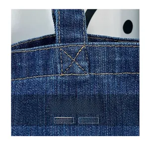 Detailed macro view of yellow X-shaped reinforced stitching on dark denim handbag texture