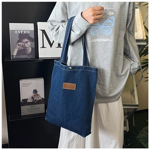 Detail of dark blue denim tote bag with leather patch logo shown on a model