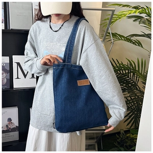 Détail du sac cabas en denim bleu avec étiquette en cuir marron porté par un mannequin