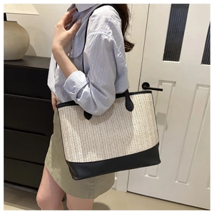 Detailed view of woven straw tote bag with black faux leather handles and bottom trim