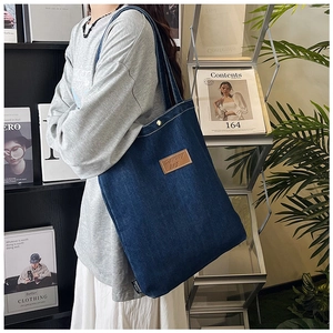 Detailed view of the dark blue denim tote bag with a brown leather logo tag and contrast stitching