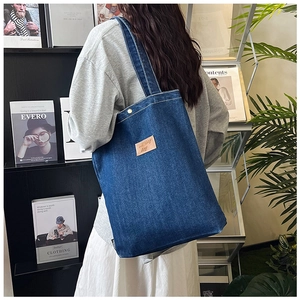 Détail du cabas en denim bleu avec écusson en cuir porté par un mannequin dans un salon