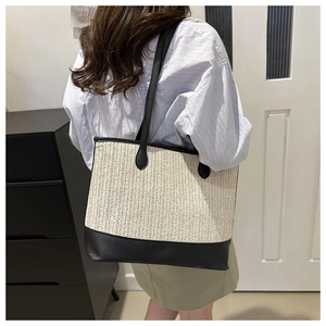 Detail of the woven texture and black leather straps on the beige straw tote bag