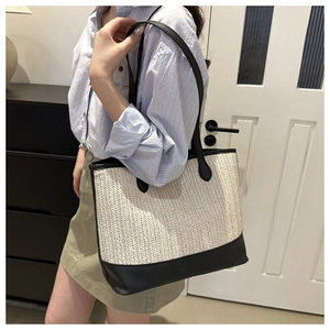Detail view of woven straw tote bag with black leather straps on a female model