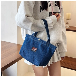 Detail of blue denim tote bag with 23 embroidery, snap closure and thick handles