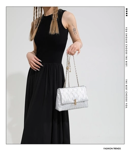 Silver quilted crossbody bag with gold chain strap shown on model in black dress